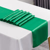 A vibrant green satin table runner is neatly folded and draped across a white tablecloth.