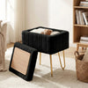 A black faux fur ottoman with a wooden lid and gold metal legs sitting on a light rug.