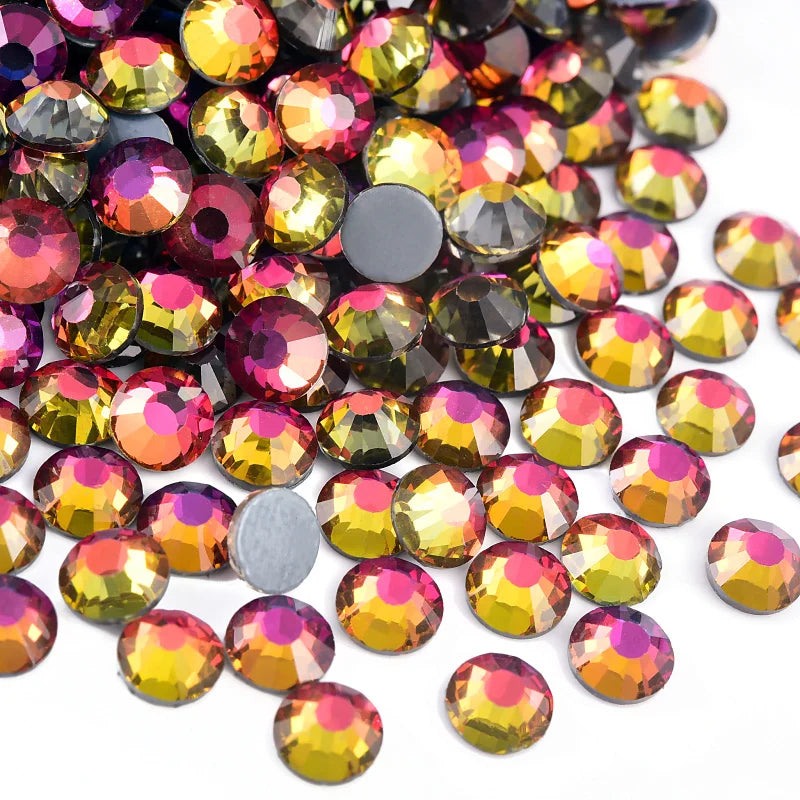 A close-up view of various flatback glass rhinestones in shades of gold, pink, and green scattered on a white background.