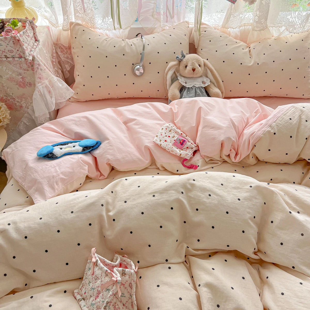 A pink polka dot duvet cover set with matching pillowcases and a stuffed bunny toy on a bed.