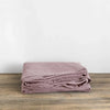 A stack of mauve pure linen flat sheets folded neatly on a wooden surface.