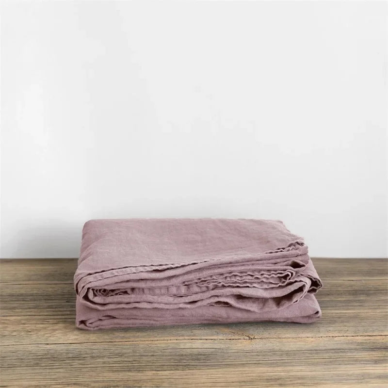 A stack of mauve pure linen flat sheets folded neatly on a wooden surface.