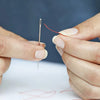 Hands holding a stainless steel needle and a red thread for embroidery or knitting.