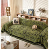 A moss green chenille sofa slipcover draped on a light rug in a bright room with slatted blinds and wooden shelving.