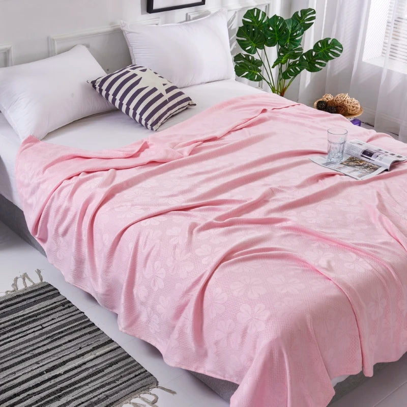 Pink bamboo fiber cooling blanket draped over a white bed with pillows and a striped rug.