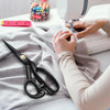 Hands are using professional heavy duty fabric scissors to cut fabric on a sewing table.