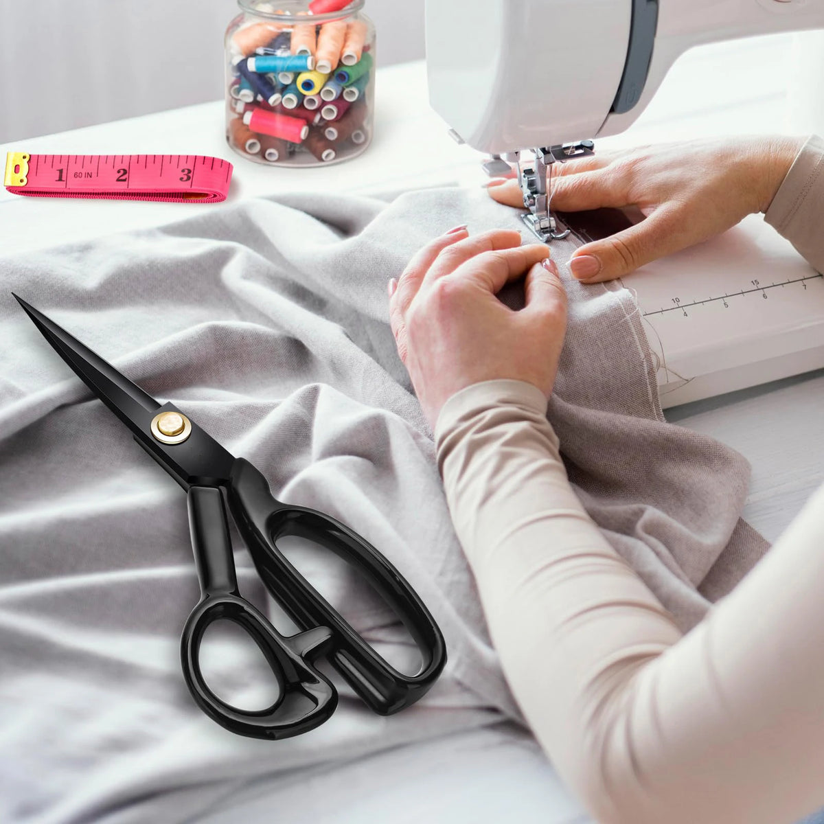 Hands are using professional heavy duty fabric scissors to cut fabric on a sewing table.