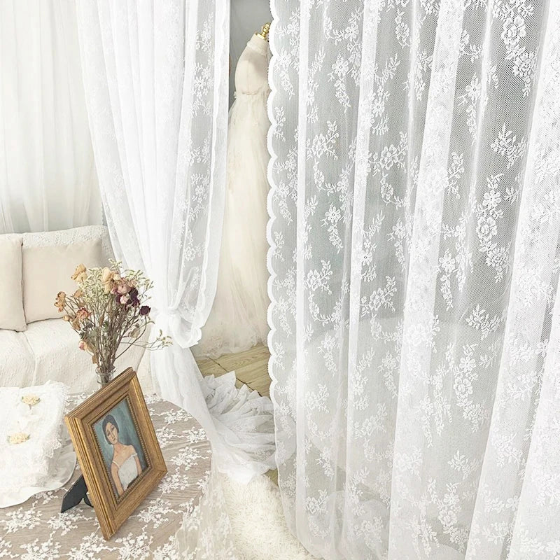 White sheer floral lace window curtains hanging in a bright room with a wooden picture frame.