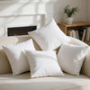 A collection of white throw pillows arranged on a light-colored sofa near a fireplace.