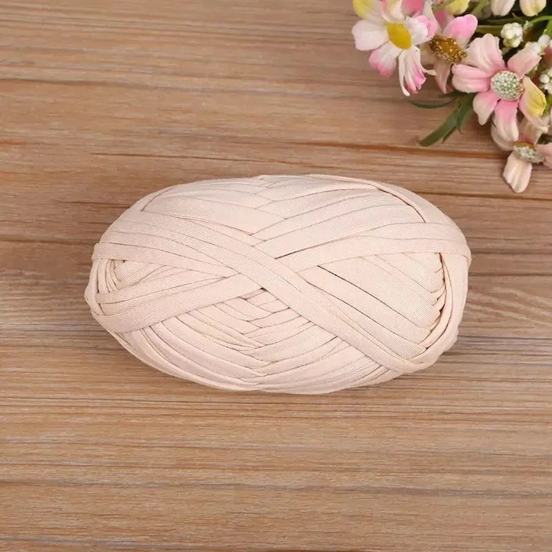 A ball of light pink flat thread yarn for crafting and sewing placed on a wooden surface.