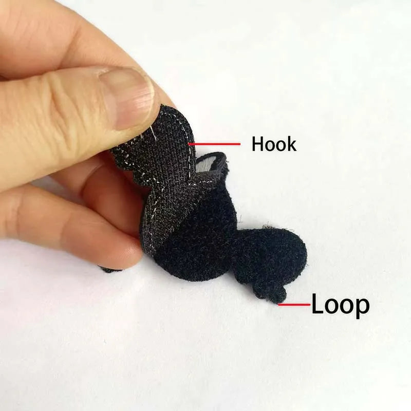 A hand holds a black felt embroidery patch showing a hook and loop for sewing.