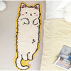 A cream-colored decorative cat mat with pink accents and yellow trim lying on a light beige fabric.