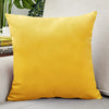 A bright yellow velvet cushion cover resting on a light-colored sofa.