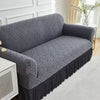 A dark gray jacquard stretch sofa cover draped over a sofa, featuring an intricate geometric pattern.