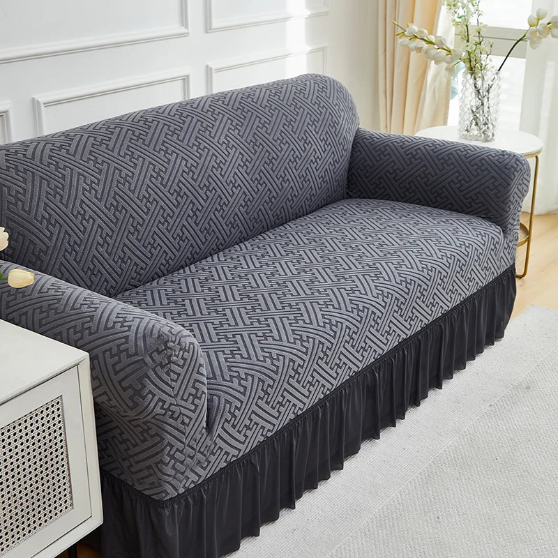 A dark gray jacquard stretch sofa cover draped over a sofa, featuring an intricate geometric pattern.