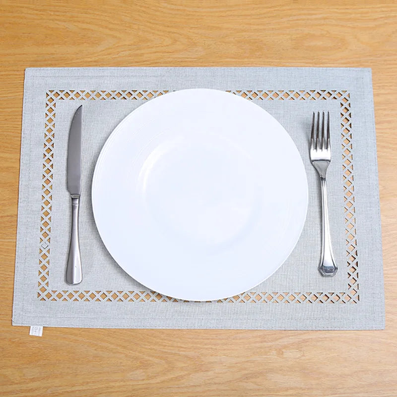 A white dinner plate, fork, and knife are placed on a gray linen placemat with a woven pattern.