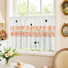 White lace cafe curtain with orange floral embroidery and black butterfly appliqués hanging in a window.