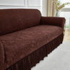 A dark brown jacquard stretch sofa cover featuring an ornate floral pattern and a ruffled hem.