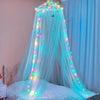 A sheer blue mosquito net bed curtain draped over a bed, decorated with glowing fairy lights and butterflies.