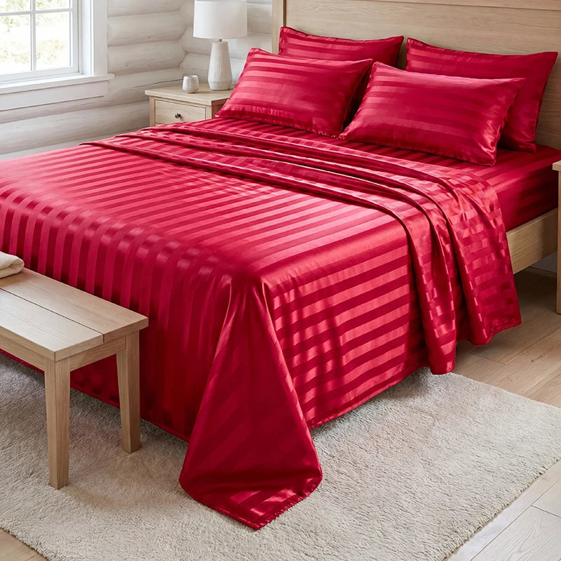 A vibrant red satin bedding set with vertical stripes is displayed on a bed, next to a wooden bench and a light rug.