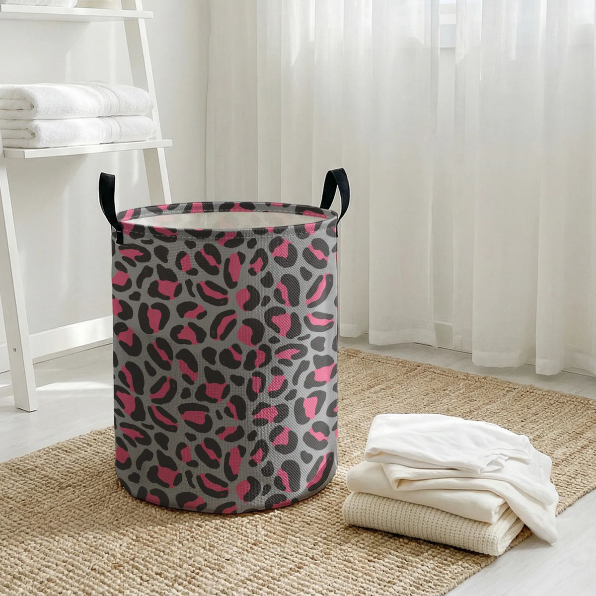 A gray and pink leopard print foldable laundry basket sitting on a woven rug near a window.