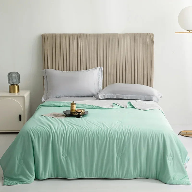 A light mint green ice silk comforter is displayed on a bed with a neutral upholstered headboard and white bedding.