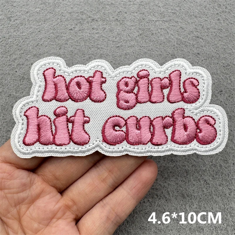 Pink embroidered patch with the text hot girls hit curbs on a gray background