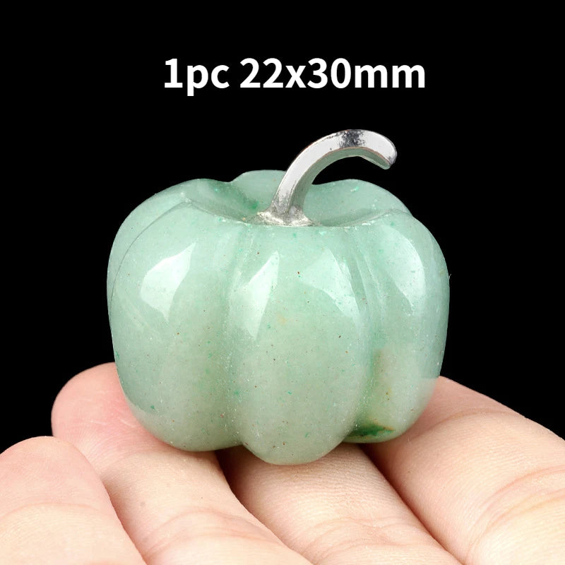A smooth, light green natural stone pumpkin figurine is held in a hand against a black background.