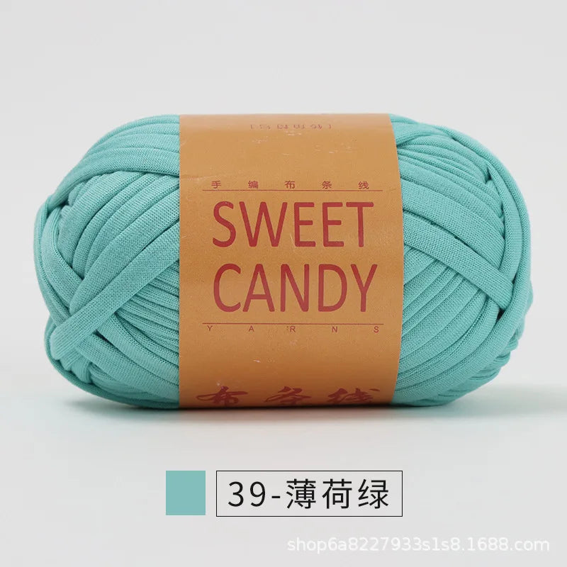 A ball of teal colored hand-dyed fabric strip yarn labeled Sweet Candy