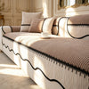 A beige striped chenille pleated sofa cover with black trim and pillows in a bright room.
