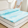 A person is placing a blue and white cooling memory foam mattress topper onto a white bed frame.