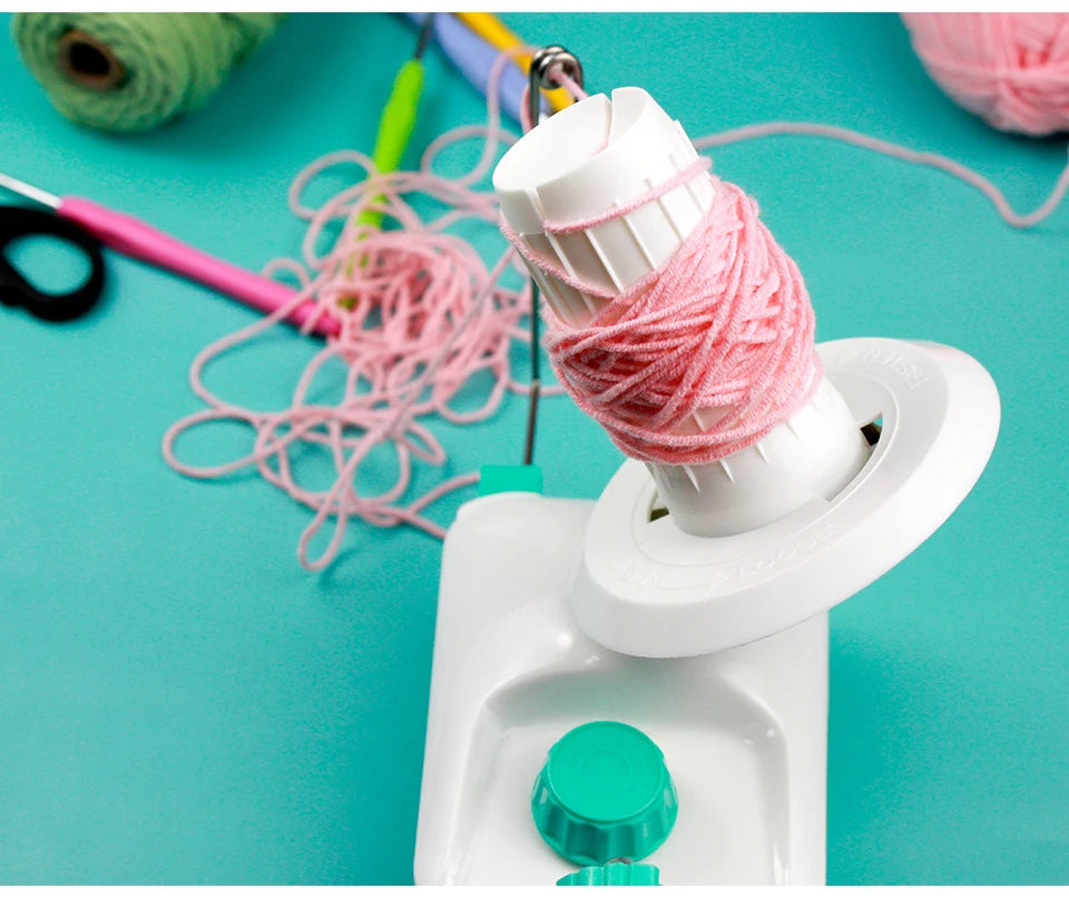 A white hand-operated wool yarn winder is shown with pink yarn being wound onto it on a teal background.