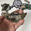 A hand holds several embroidered military patches including an Air Force patch and various insignia.