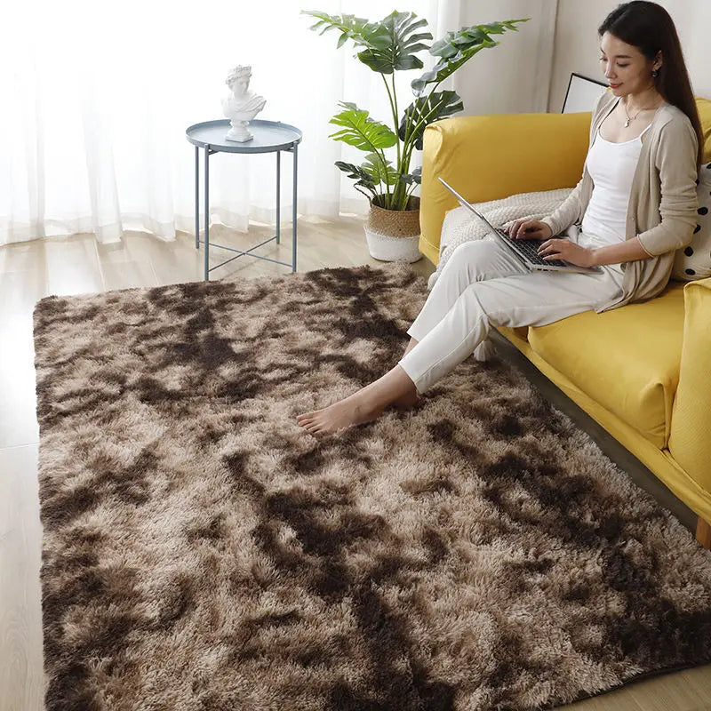 A woman sits on a yellow sofa indoors with a large brown faux fur rug and a potted plant in the background.