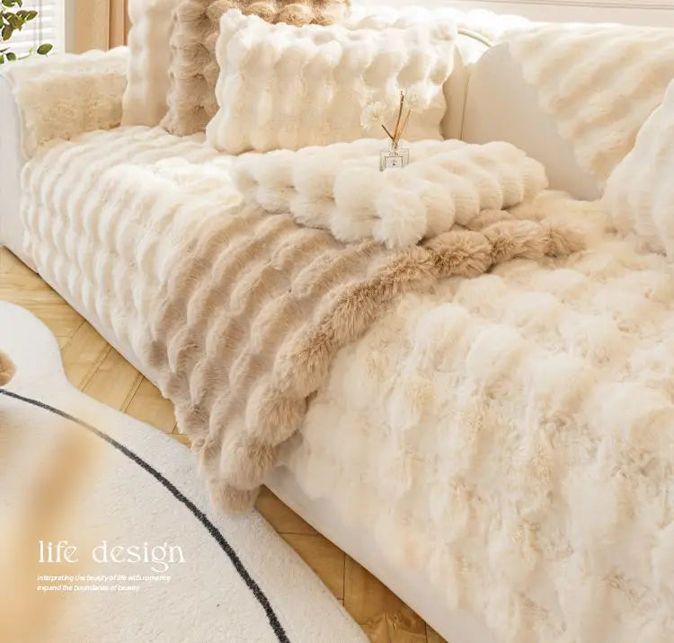 A luxurious beige plush rabbit fur sofa cushion cover draped over a light-colored sofa.