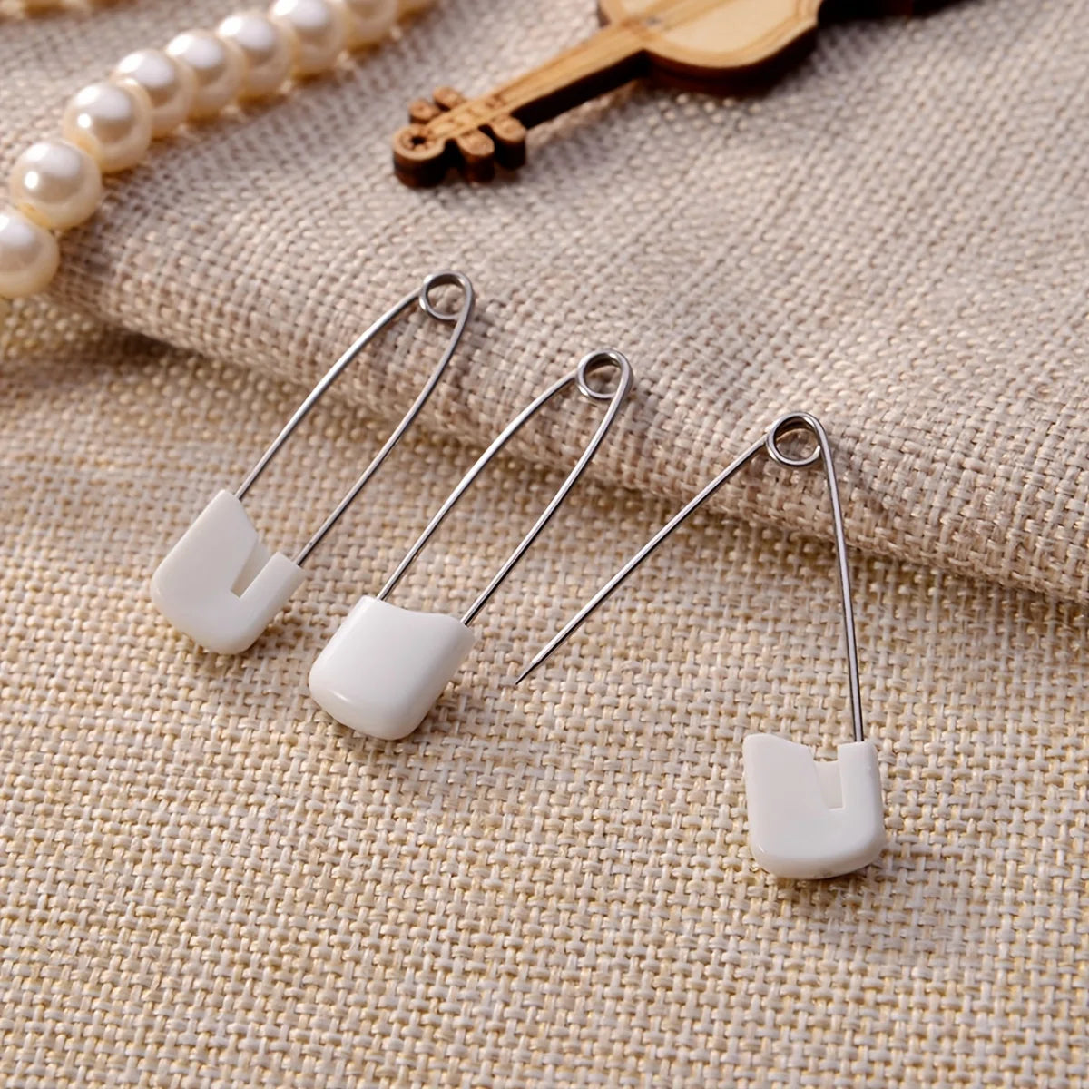 A collection of stainless steel diaper pins with safety locking closures resting on a beige fabric.