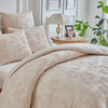 A beige luxury quilt duvet set displayed on a bed with white walls and a table lamp.