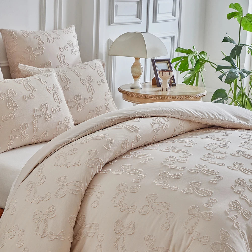 A beige luxury quilt duvet set displayed on a bed with white walls and a table lamp.