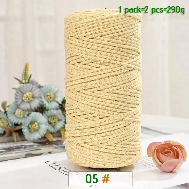 A spool of beige medium-thick hand-woven cotton yarn for crafting, next to some light blue flowers.
