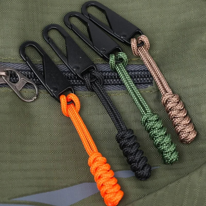 A collection of detachable zipper pull sliders in various colors and materials attached to a green fabric background.