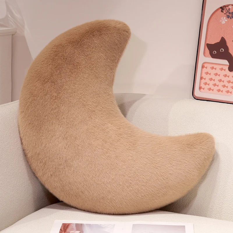 A beige moon-shaped throw pillow resting on a white surface.