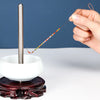 A hand is using a thin wire or needle to thread beads onto a stainless steel tool resting on a dark base.