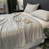 A white reversible cooling quilt is displayed on a bed with gray bedding and pillows.