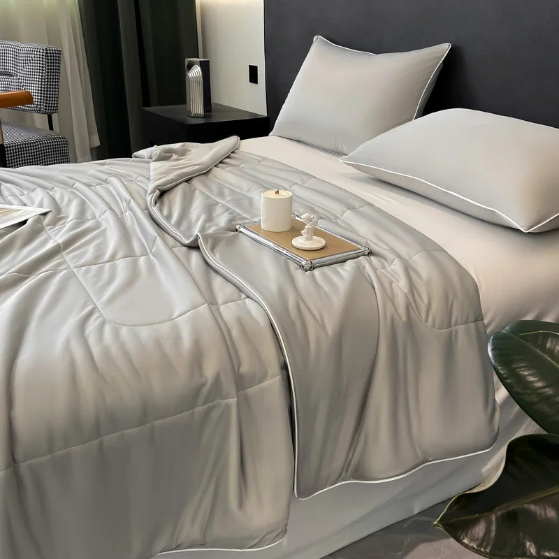 A white reversible cooling quilt is displayed on a bed with gray bedding and pillows.