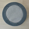 A round, gray fabric slipcover for an ottoman footrest with ribbed edges.