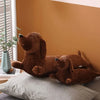 A brown corduroy dachshund body pillow resting on a gray cushion against an orange wall.