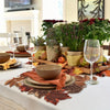 A rustic farmhouse maple leaf table runner laid on a white tablecloth with autumnal foliage and floral arrangements.