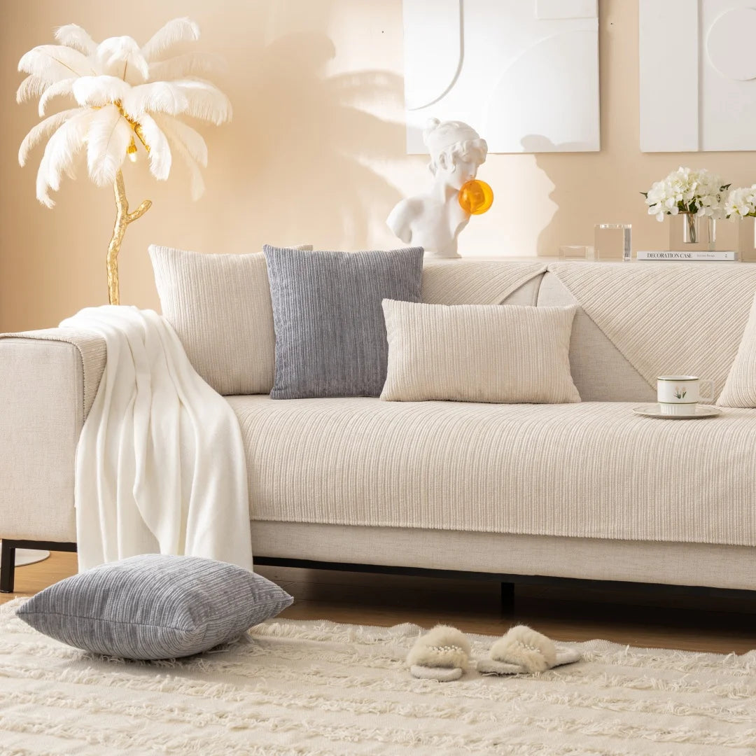 A beige sofa with gray and cream cushions, a white sculpture, and a white throw blanket on a light rug.