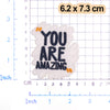 White embroidered patch with black text YOU ARE AMAZING and small orange accents on a grid background.