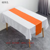 White tablecloth with an orange satin table runner displayed on a gray floor.